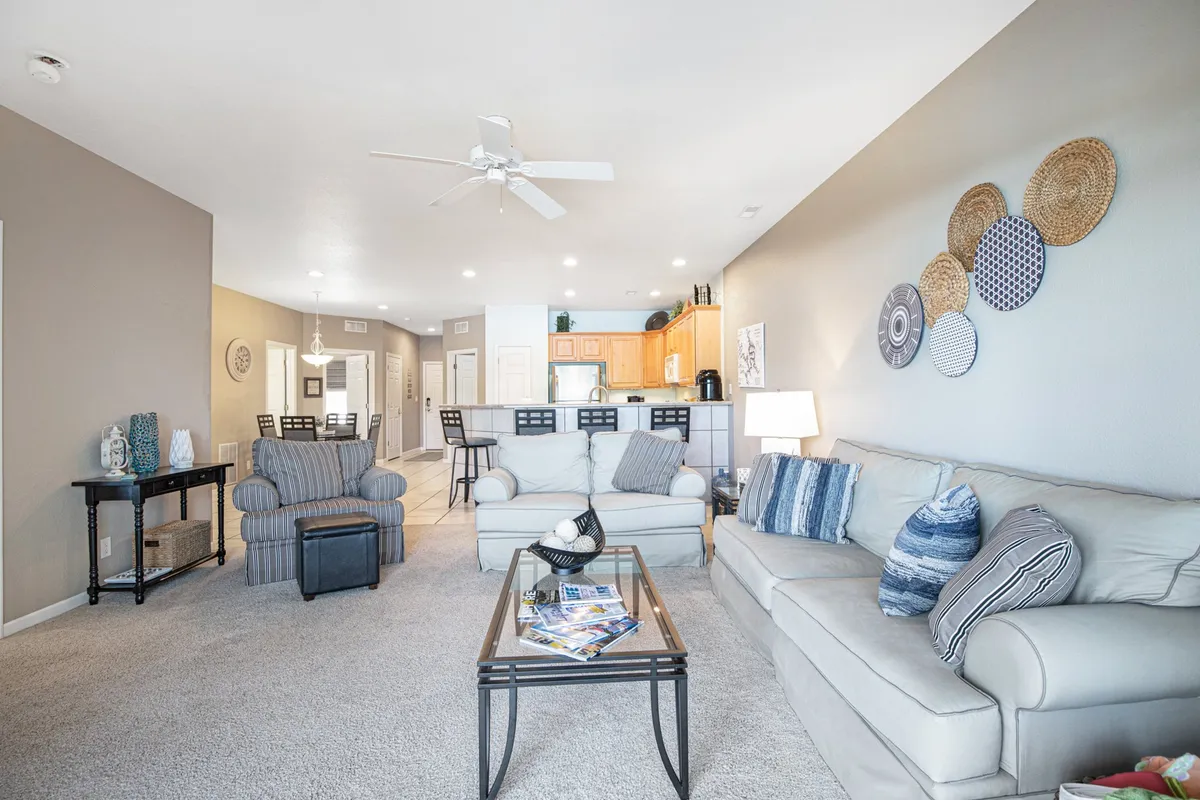 This image features a welcoming, open-concept living area with a cozy sofa, coffee table, decorative wall art, and the kitchen area visible in the background. The setup is ideal for socializing, relaxing, or entertaining guests, and highlights the interconnectedness of the living and kitchen spaces.
