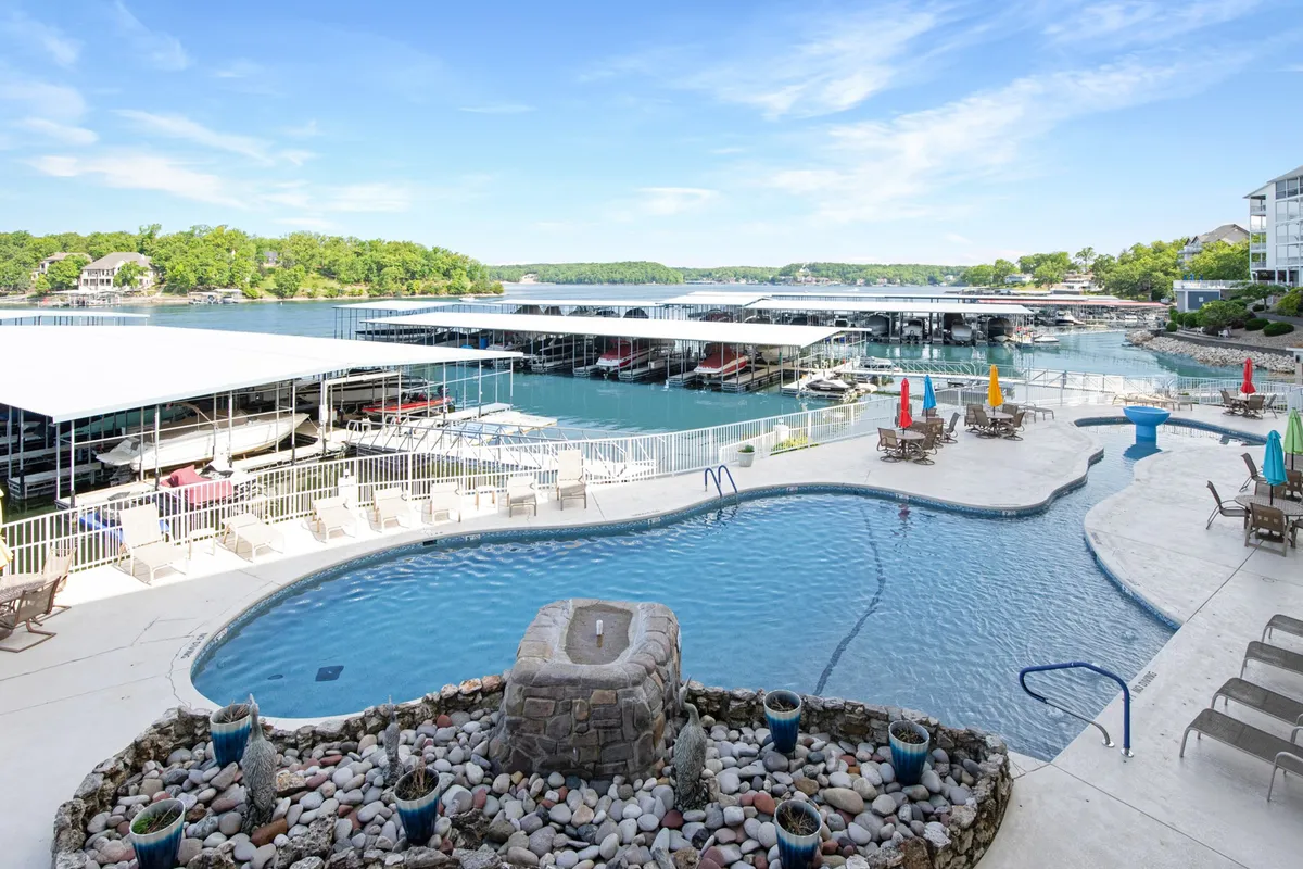 A wide exterior shot showcasing the swimming pool, marina, lush landscaping, and a beautiful fountain. The marina, with boats docked and ready, is visible in the background, emphasizing the close connection to water activities and the convenience of boating access.