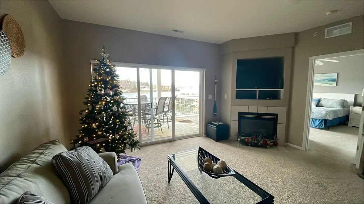 An interior scene showcasing a cozy living area with a Christmas tree, fireplace, television, and large glass sliding doors leading out to the balcony. The view from the balcony hints at additional scenic beauty outside.