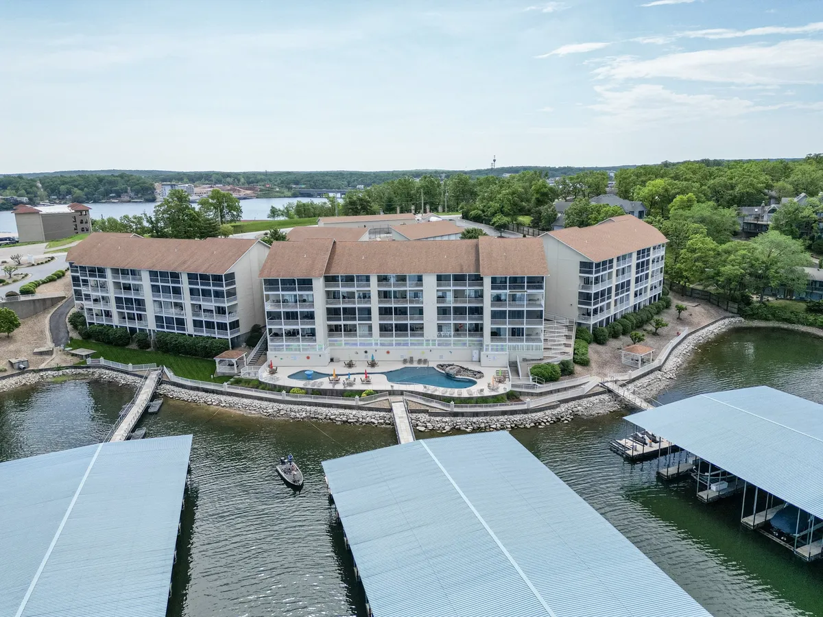 This image showcases the vibrant lakefront setting with a clear view of the waterfront building, the swimming pool area, nearby boat docks, and lush greenery. It captures the recreational amenities right at the water’s edge, including places for swimming, boating, sunbathing, picnicking, and strolling along the scenic lakeshore.