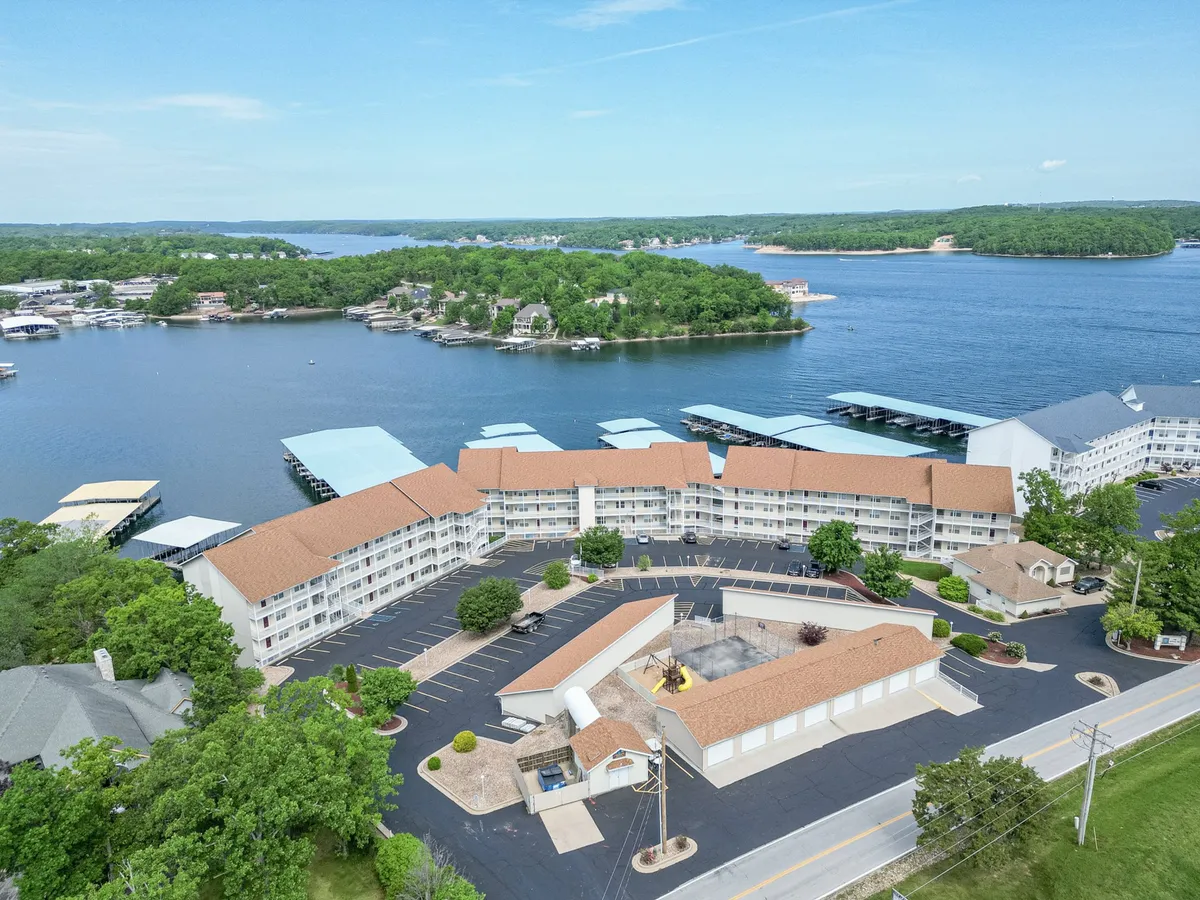 A panoramic exterior shot featuring the lake, the adjacent hotel structure, lush greenery, and boats docked in the marina. The relaxed setting invites families and groups to gather by the shore, participate in water sports, or simply enjoy beautiful sunset views over the lake.