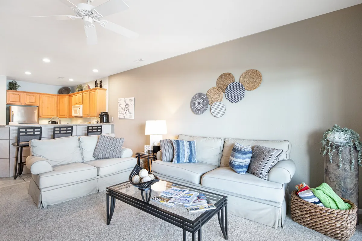 A cozy, open-plan living area with comfortable sofas, a coffee table, and decorative wall art, with the kitchen visible in the background. The space is uncluttered and designed for single-level living, allowing for easy movement and relaxation.