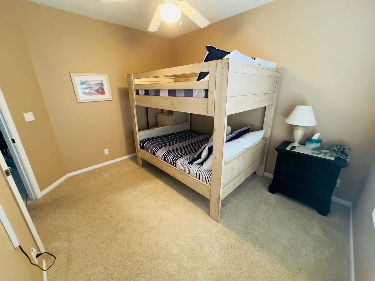 A cozy additional sleeping space with a sturdy bunk bed, soft bedding, a nightstand with a lamp, and playful wall art. The scene is inviting, suggesting the area is perfect for kids or extra guests to enjoy a restful night or family bonding before bed.