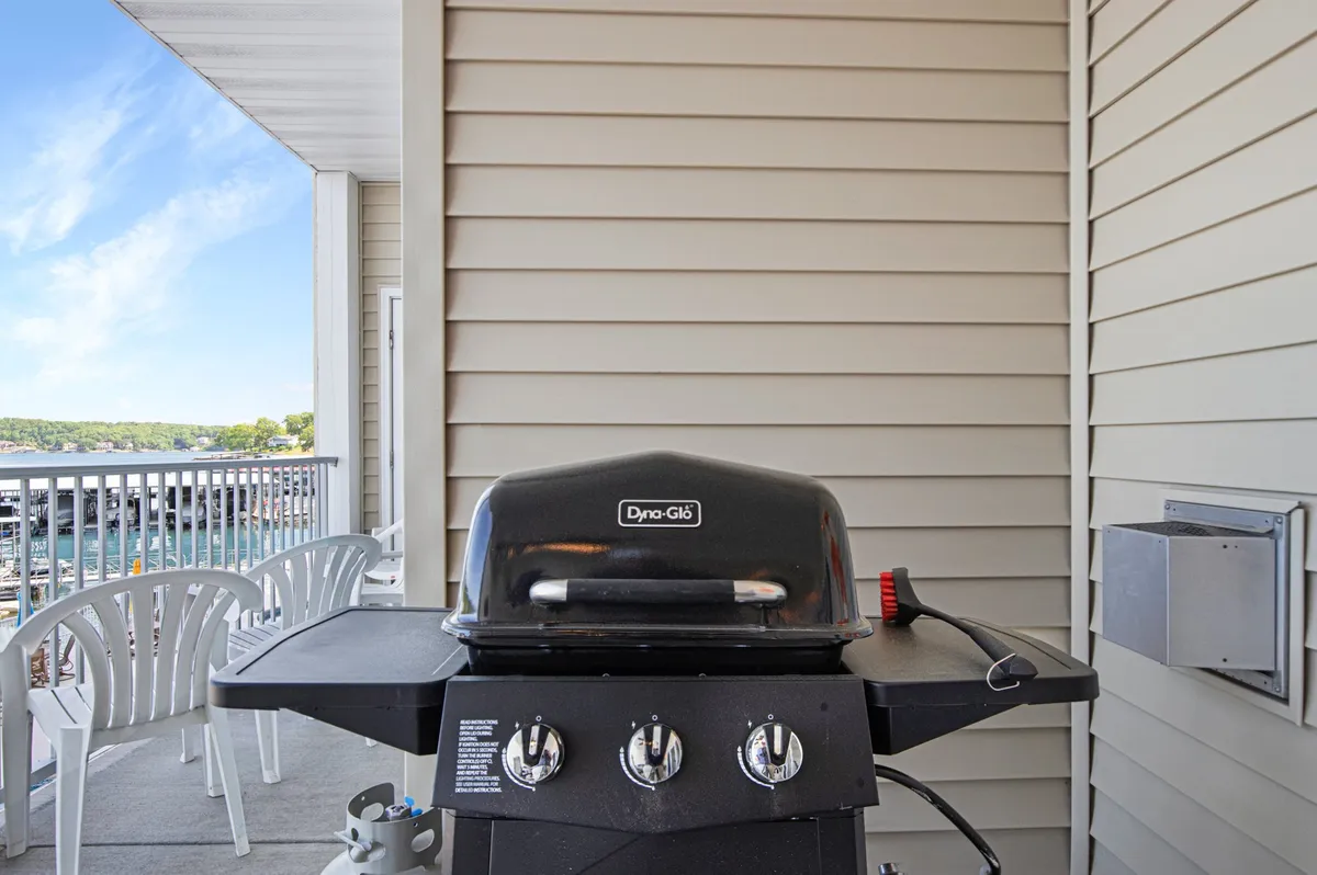 An outdoor space featuring a grill, comfy seating, and a clear view of the water. The scene suggests relaxed barbecues and alfresco dining, with the backdrop of the lake enhancing the sense of a vibrant, social, and inviting outdoor living area.