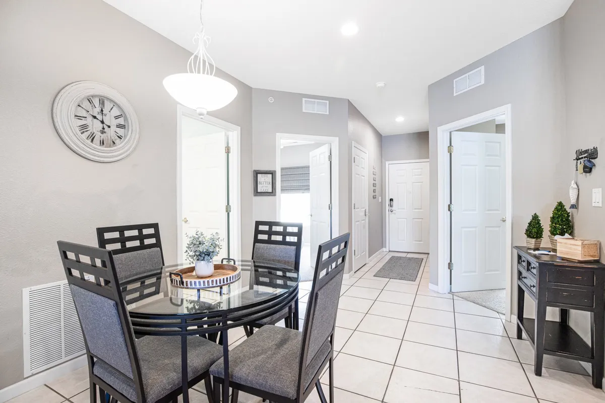 This image features a cozy dining table and entryway area, with a decorative clock and side table with plants. The table suggests a welcoming spot for gathering, while the entryway is visible, giving a sense of organized space and thoughtful touches.